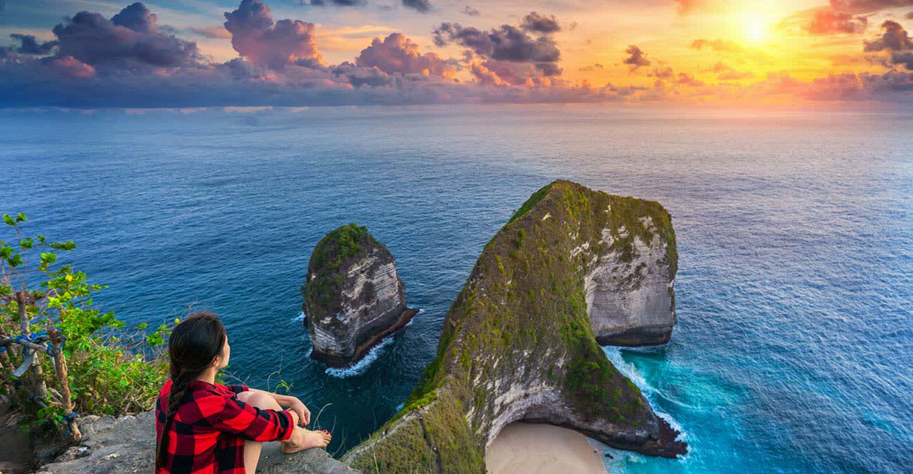 Woman is watching the scenery while sitting on a rock in Bali