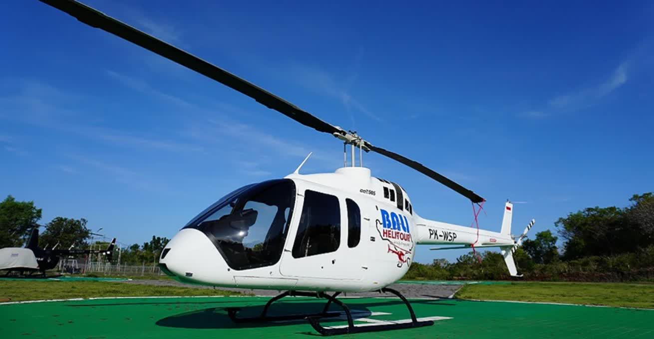 A white helicopter with the logo of the Bali Helitour company is standing in the parking lot