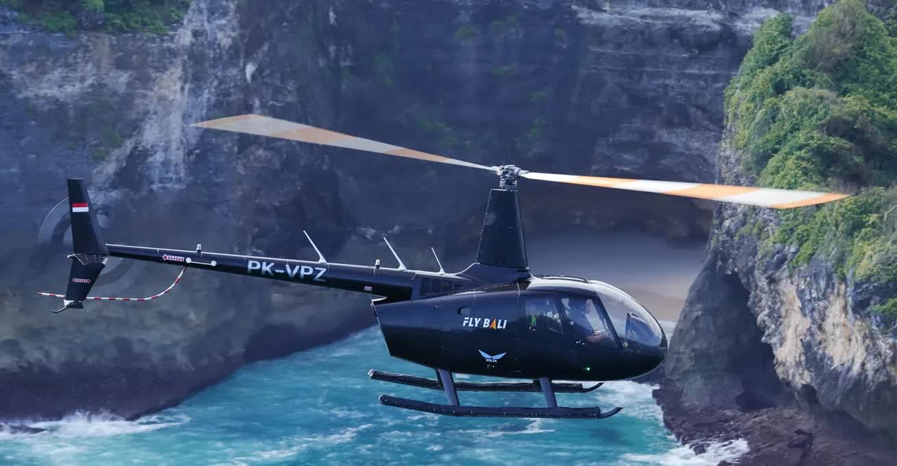 A black helicopter from Fly Bali Heliport is flying between the rocks